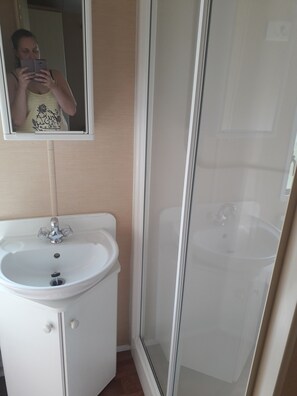 Et badeværelse med en hvid vask, et spejl og en brusekabine med glas.