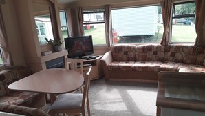 A compact RV interior with a sofa, a table, and a TV. - 3-bedroom Caravan at Thorness bay (Cowes)