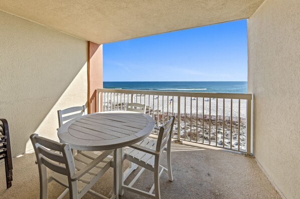 A balcony with a table and chairs, overlooking a beach with a fence and ocean view.