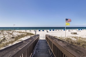 A wooden boardwalk leading to a beach with tents and a flag.