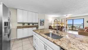 A modern kitchen with white cabinets, granite countertops, and a stainless steel refrigerator. - Harbour Place 313 (Orange Beach)
