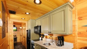A compact kitchen with wooden walls, a granite countertop, a sink, a stove, and a microwave.