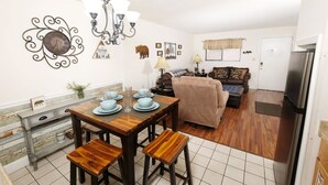 A dining area with a wooden table set for four, a sofa, and a television in the background. - Oak Square 305 - Ask About Free Attraction Tickets! (Gatlinburg)