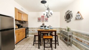 A kitchen with wooden cabinets, a stainless steel refrigerator, a dining table with stools, and a decorative wall piece. - Oak Square 305 - Ask About Free Attraction Tickets! (Gatlinburg)