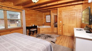 A wooden cabin bedroom with a bed, desk, chair, and a bathroom with a bathtub.