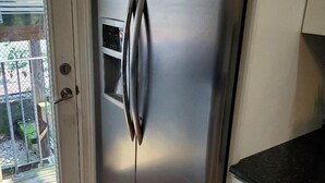 Un réfrigérateur en acier inoxydable dans une cuisine dotée d’un plancher en bois et de meubles blancs.