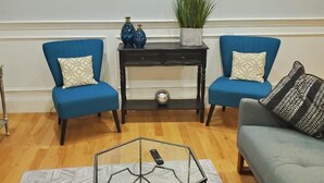 Un salon avec deux fauteuils bleus, un canapé gris, une table basse noire et un tableau accroché au mur.