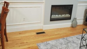 Un salon avec une cheminée, un téléviseur fixé au mur et un tapis à motifs.