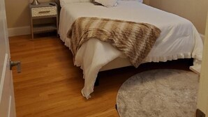 Une chambre à coucher avec un lit, une lampe de chevet, un tableau décoratif au mur et une fenêtre avec des stores.