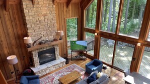 Un salón acogedor con chimenea de piedra, un ventanal con vistas a un bosque y una zona de estar confortable.