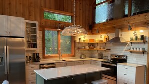 Una cocina moderna con una isla grande, armarios de madera y vistas al bosque a través de amplios ventanales.
