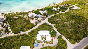 An aerial view of a coastal property with multiple buildings, surrounded by dense vegetation and a beach. - Beautiful Home by Taylor Bay Beach (Providenciales)