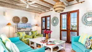 A living room with teal sofas, a coffee table with board games, and a TV displaying a beach scene. - Beautiful Home by Taylor Bay Beach (Providenciales)