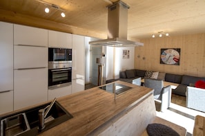 A modern kitchen with built-in appliances, a wooden ceiling, and a cozy seating area with a sofa and a table. - Superior Chalet # 61 with Sauna & Whirlpool (St. Georgen am Kreischberg)