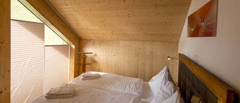 Una habitación con paneles de madera, dos camas, una ventana con persianas y una lámpara de pared.
