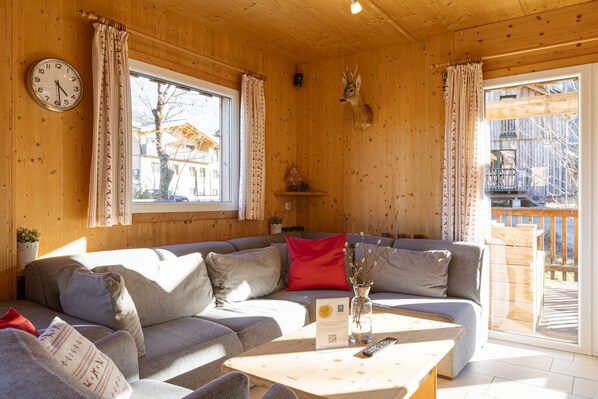 A cozy wooden cabin interior with a sofa, a coffee table, and a clock on the wall.