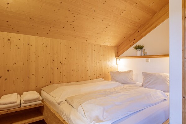Una habitación con paneles de madera, una cama, un estante con toallas y una planta pequeña en la pared.