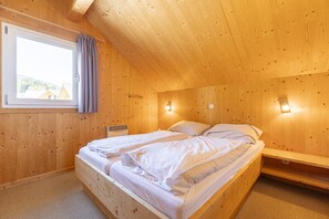 A wooden cabin bedroom with a bed, a window with curtains, and wall-mounted lights.