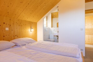 A bedroom with wooden walls, a bed with white bedding, a bedside table, and a mirror.