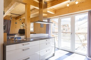 A modern kitchen with wooden beams, a stainless steel range hood, and a large sliding glass door leading to a deck.