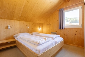 Un dormitorio de cabaña de madera con dos camas, una ventana con cortinas y una lámpara fijada a la pared.