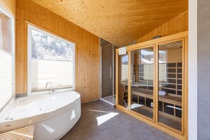 A modern bathroom with a freestanding bathtub, a glass shower enclosure, and wooden walls.