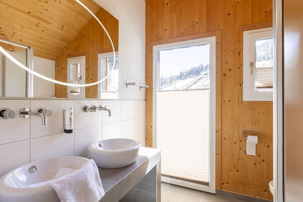 Un baño moderno con paredes de madera, un ventanal grande y un lavamanos blanco.