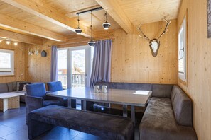 A wooden interior with a dining table, benches, and a mounted deer head.