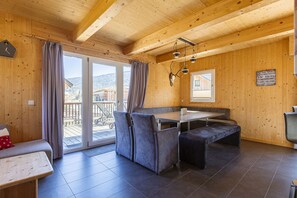 Un intérieur en bois comprenant une table à manger, des sièges rembourrés, un banc et une vue dégagée grâce à de grandes portes vitrées.