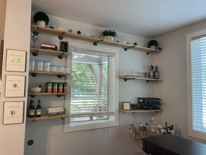A bar area with shelves holding glasses, bottles, and a sign that says "LET'S STAY IN".