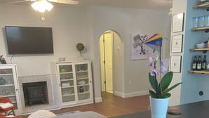 Una sala de estar moderna con chimenea, ventilador de techo, televisor montado en la pared y comedor con taburetes de bar.