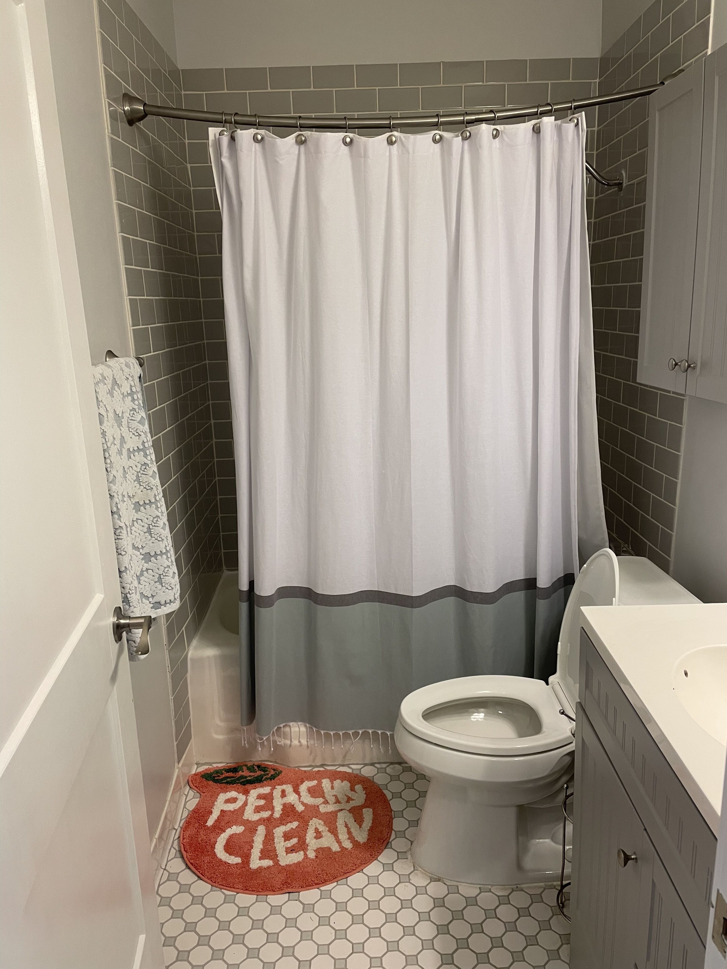 A bathroom with a shower curtain, toilet, and a rug with "PEACH CLEAN" text.