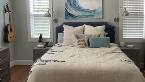Un dormitorio con una cama, una guitarra, un cuadro y dos lámparas de noche.