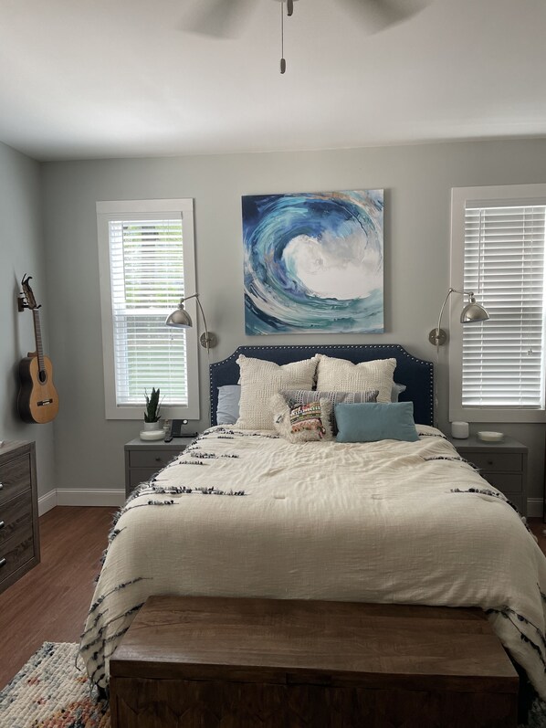 A bedroom with a bed, a guitar, a painting, and two bedside lamps.
