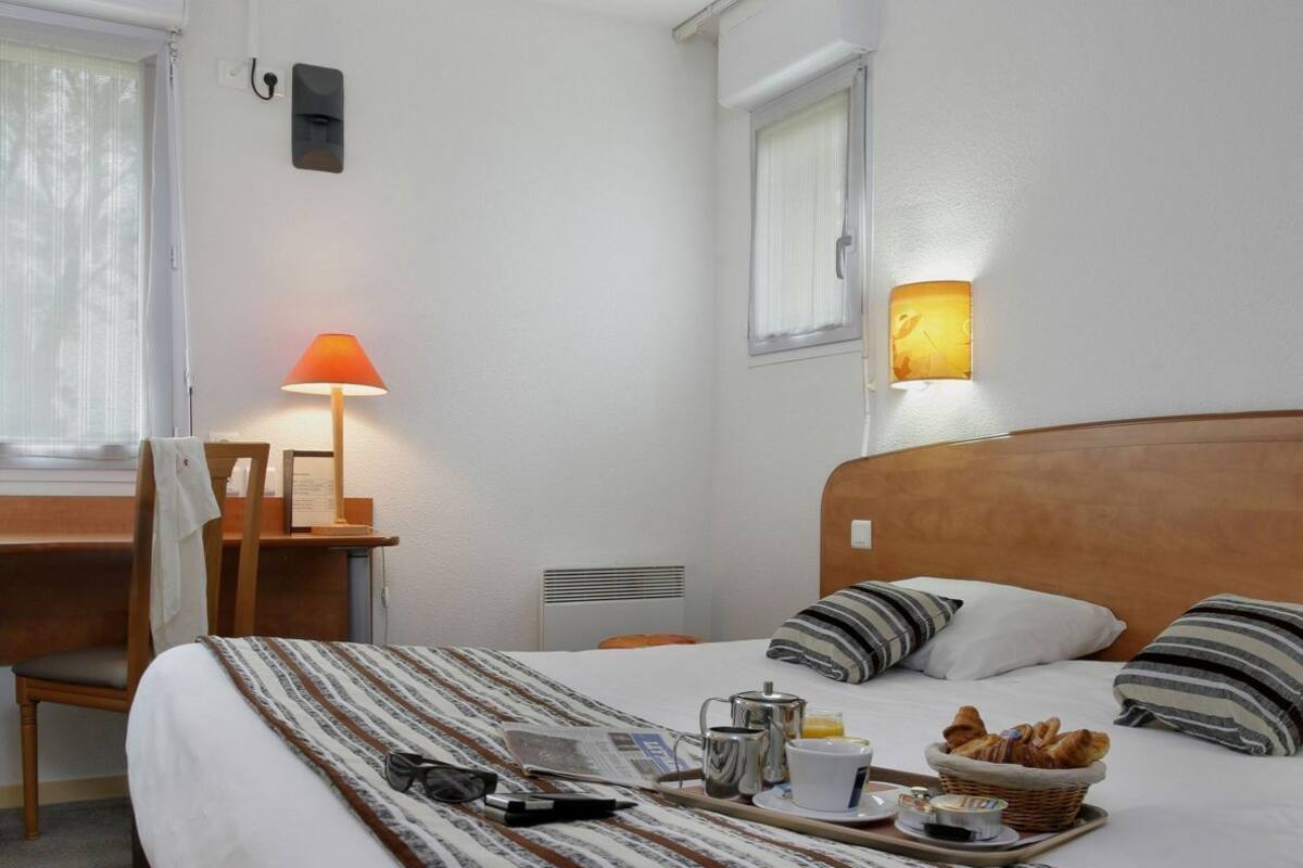 A hotel room with a bed, a desk, a chair, a lamp, and a breakfast tray.