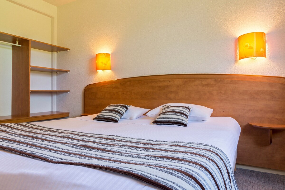 Ein Hotelzimmer mit einem hölzernen Kopfende, zwei Nachttischlampen, einer gestreiften Bettdecke und einem Nachttisch aus Holz.
