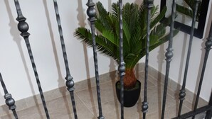 En trappe i træ med gelænder i metal, en potteplante og et flisegulv.