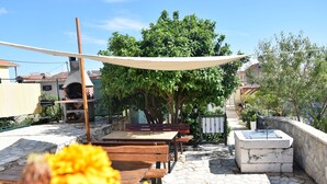 En udendørs terrasse med flisebelægning, et træbord, en grill og et vandelement.