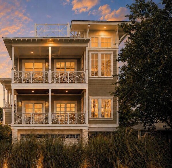 Een meerlaags huis aan de kust met balkons, grote ramen en uitzicht op zee.