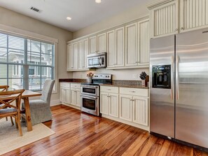 A modern kitchen with white cabinetry, stainless steel appliances, and a dining area with a wooden table and chairs.