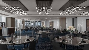 Un comedor moderno de hotel con varias mesas redondas dispuestas para comer, con vasos transparentes y servilletas.