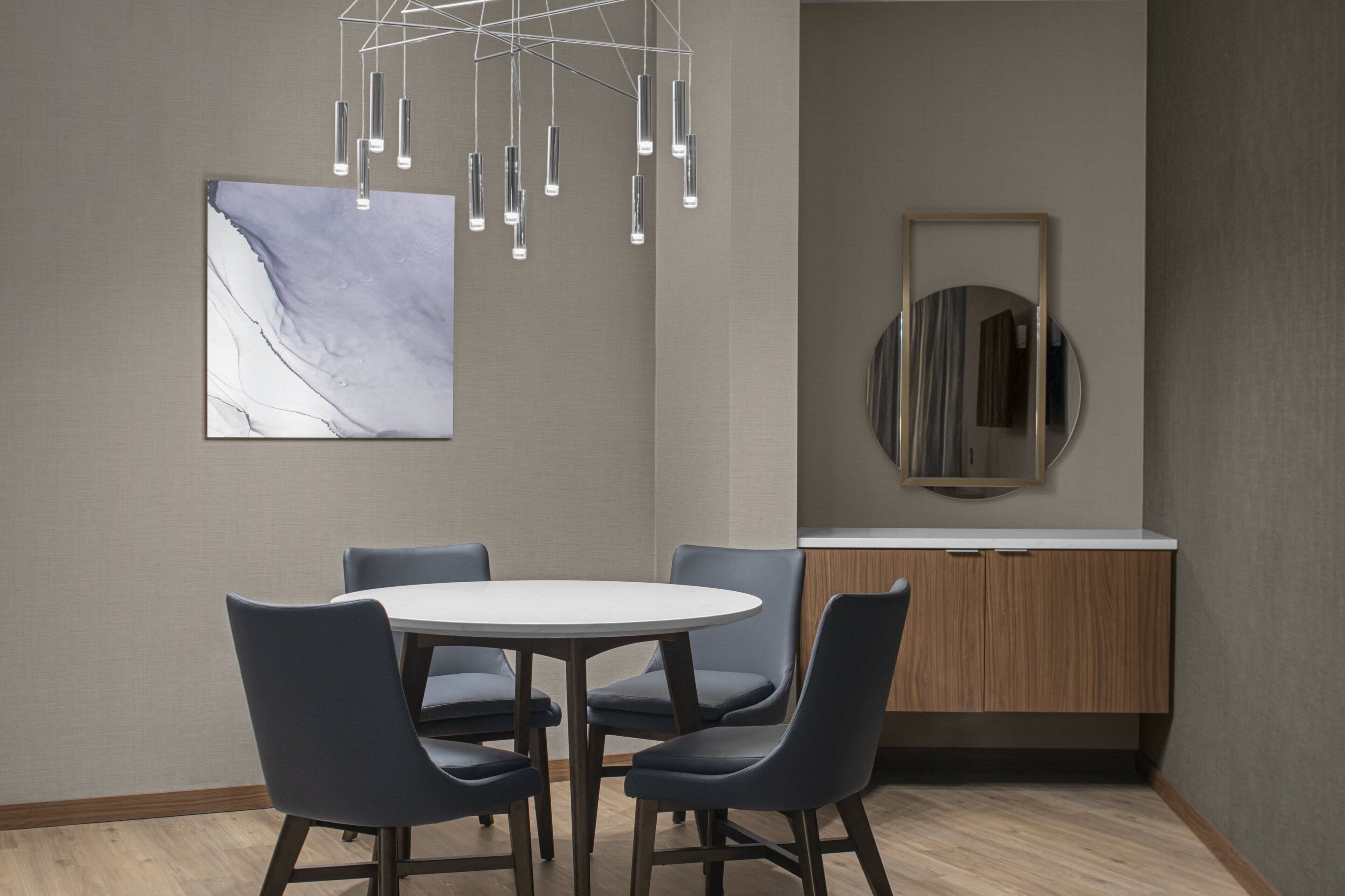Un comedor moderno con una mesa redonda, cuatro sillas, una lámpara colgante, una obra de arte de mármol y un espejo en la pared.