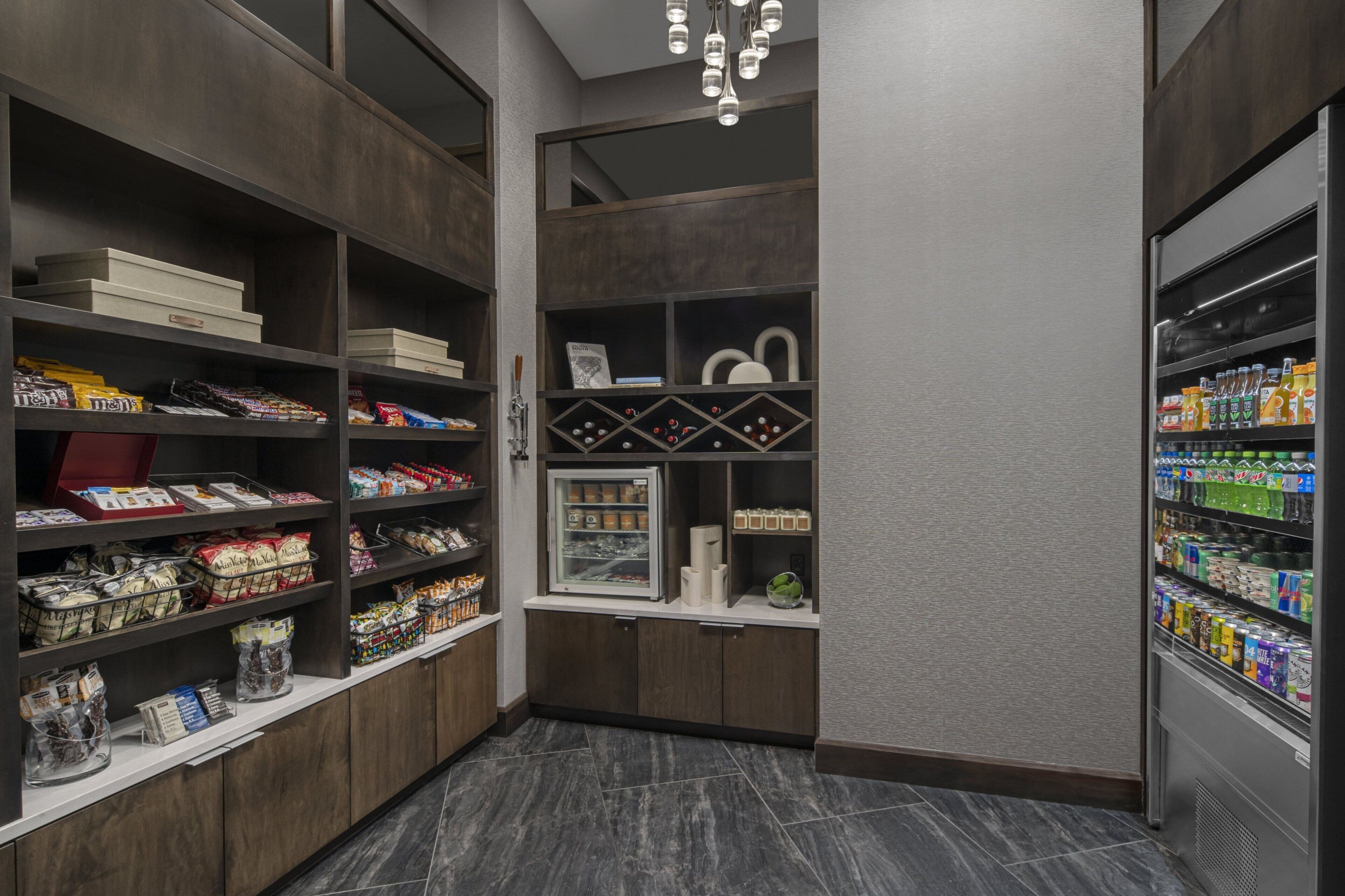 A modern hotel pantry with shelves stocked with snacks, a refrigerated display, and a beverage fridge.