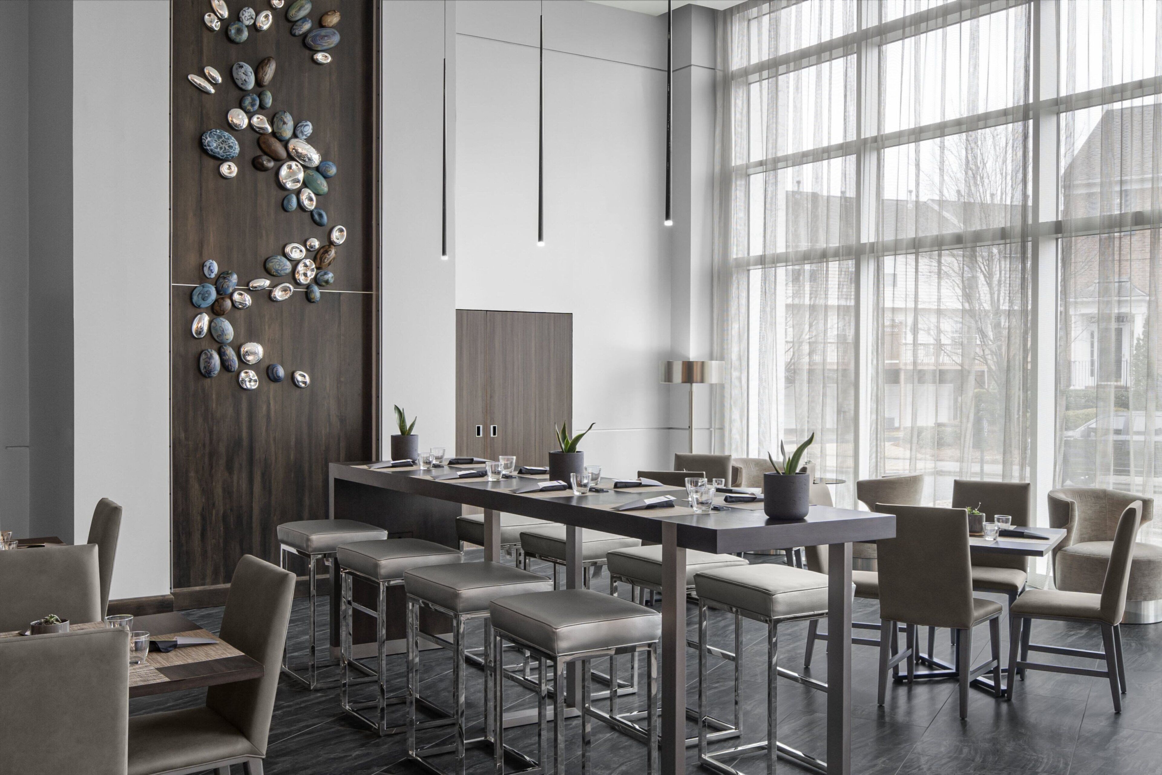 A modern dining area with a long table, multiple chairs, and a decorative wall with stones.