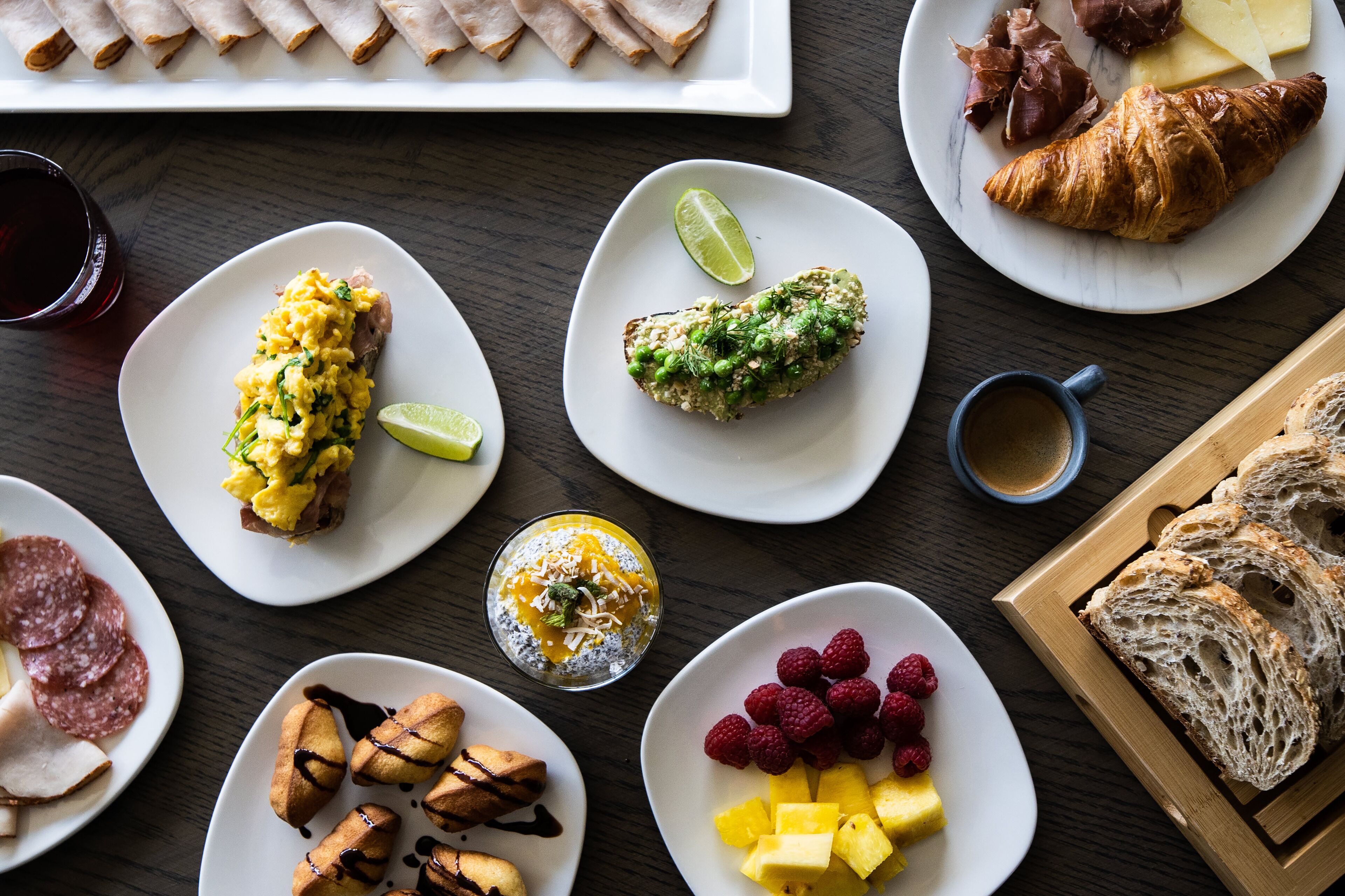 Une variété d’aliments pour le petit-déjeuner, notamment des œufs, des croissants et des viennoiseries, disposés sur une table en bois.