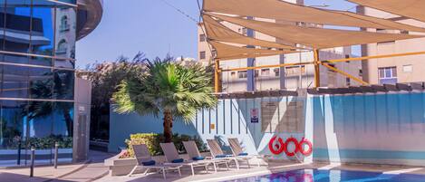 Una piscina con toldos, sillas de descanso y una palmera.