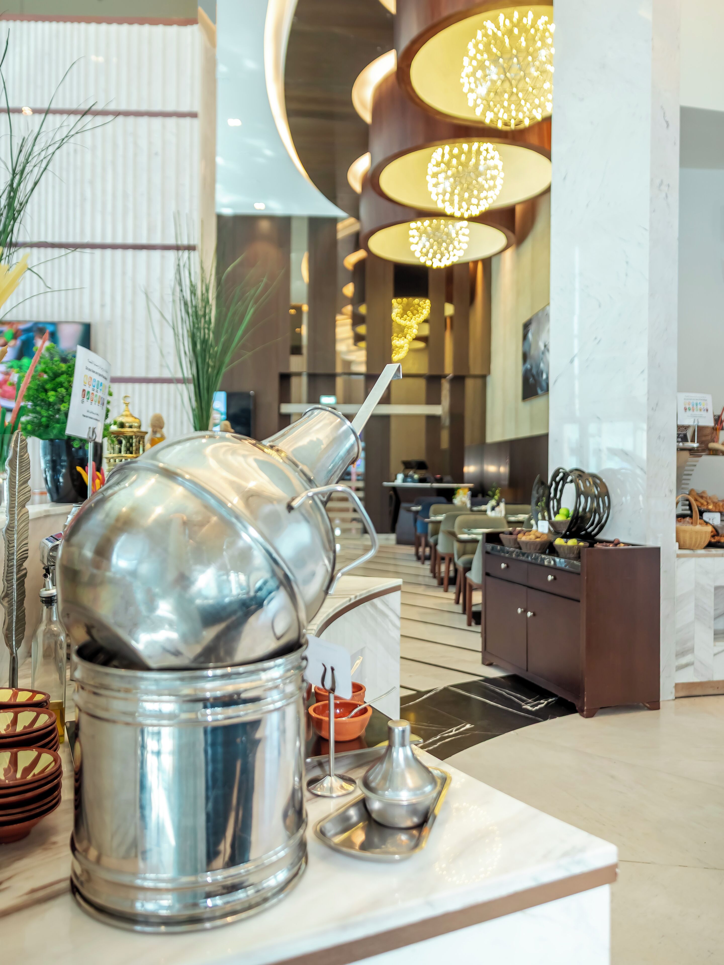 A modern hotel lobby with a buffet area, including a large silver buffet pot and a marble counter.