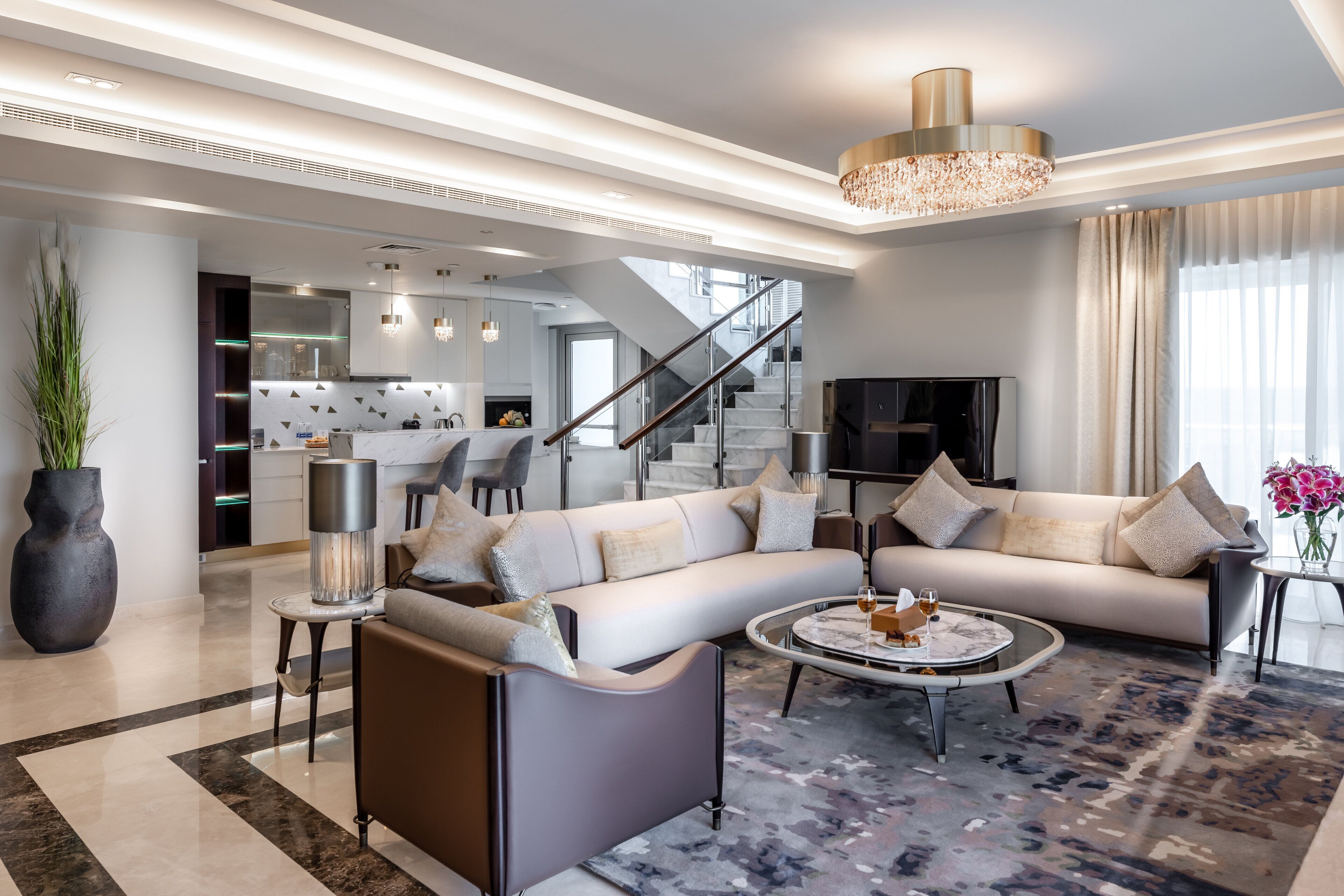 Una sala moderna con un sofá modular, una mesa de centro y una escalera que lleva a una cocina.