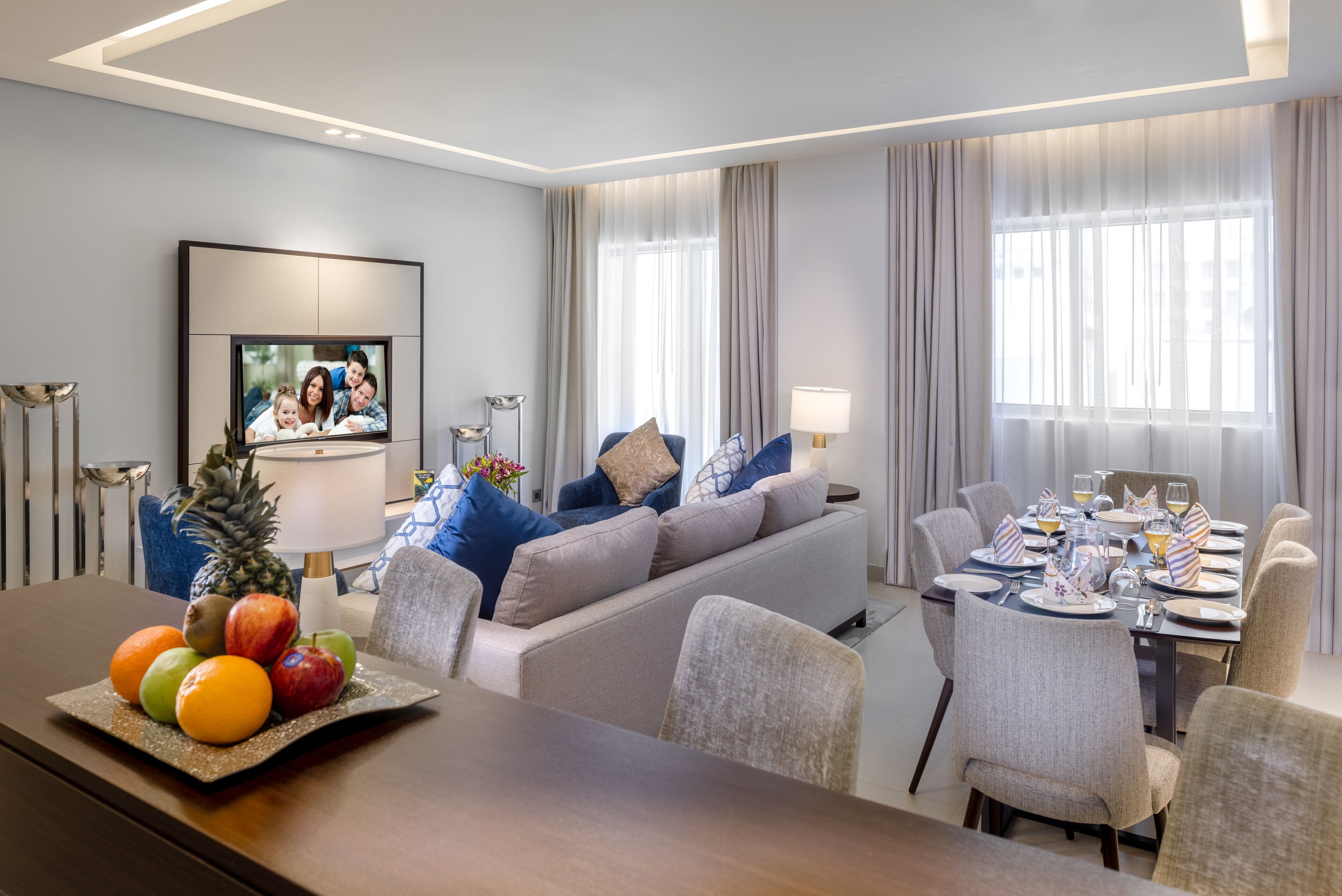 Een moderne hotelkamer met een eethoek, een zithoek, een flatscreen televisie en een schaal fruit op de tafel.