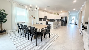A spacious kitchen with a central island, modern appliances, and a dining area with a striped rug and black chairs. - Luxury 6 bed South-Facing Pool, Game Room, 4 Miles to Disney World (Kissimmee)